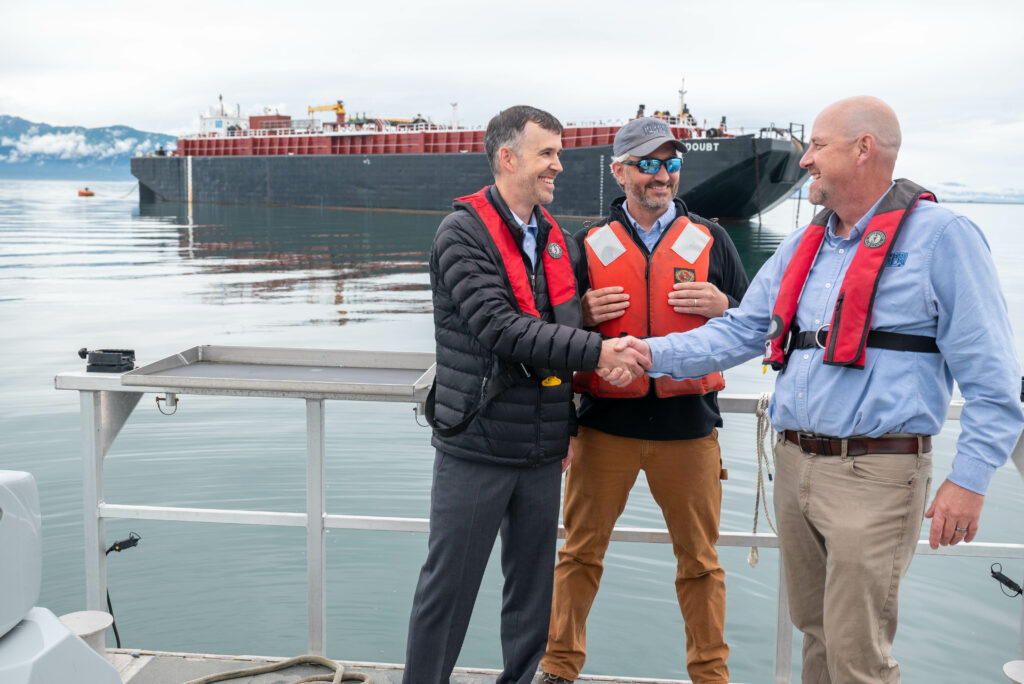 Two men shaking hands on a boat, symbolizing agreement and collaboration amidst a serene water backdrop.