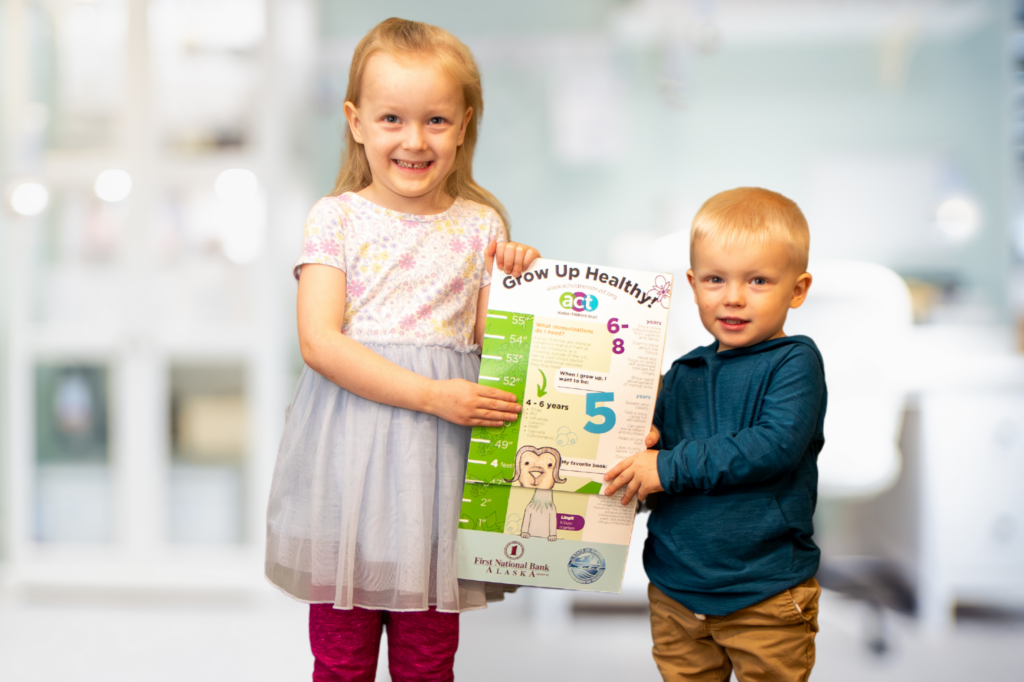 Two kids stand together, lifting a poster that features a child's image, expressing joy and enthusiasm in their project.