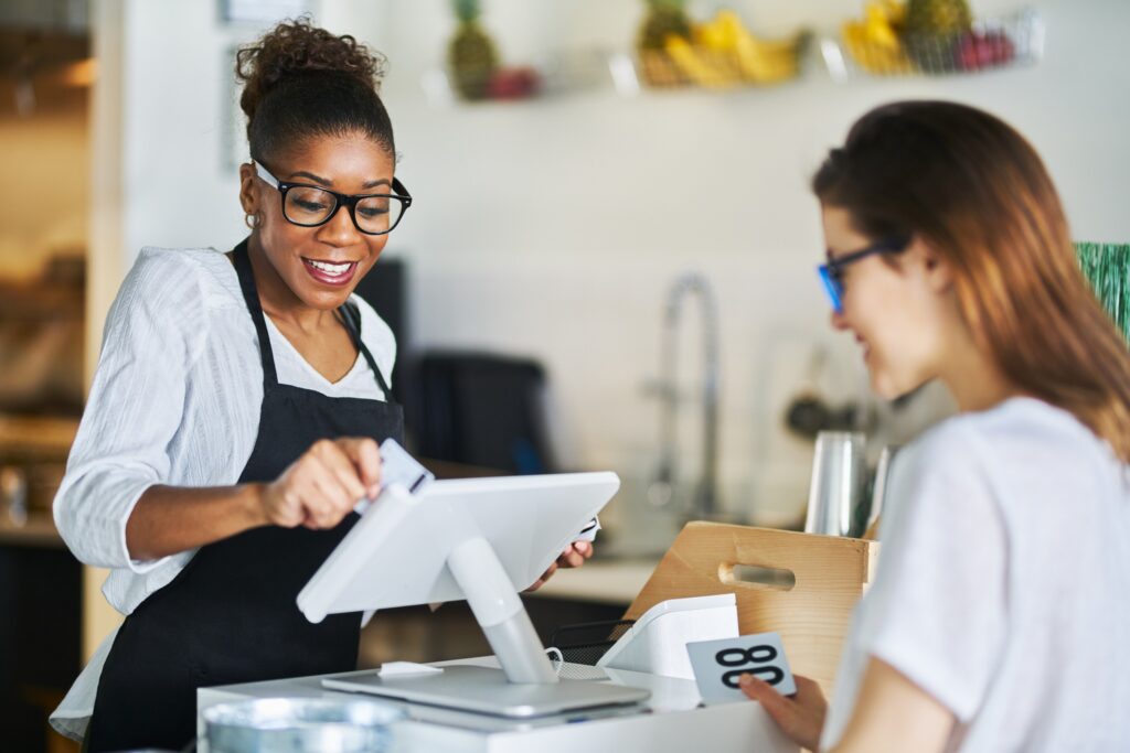 A woman in glasses speaks with a cashier, facilitating a transaction at a store checkout.