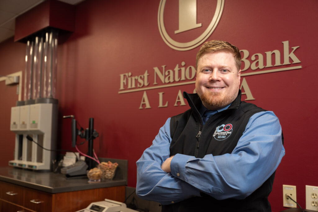 A man stands confidently in front of the First National Bank Alaska logo, showcasing the bank's identity and presence.