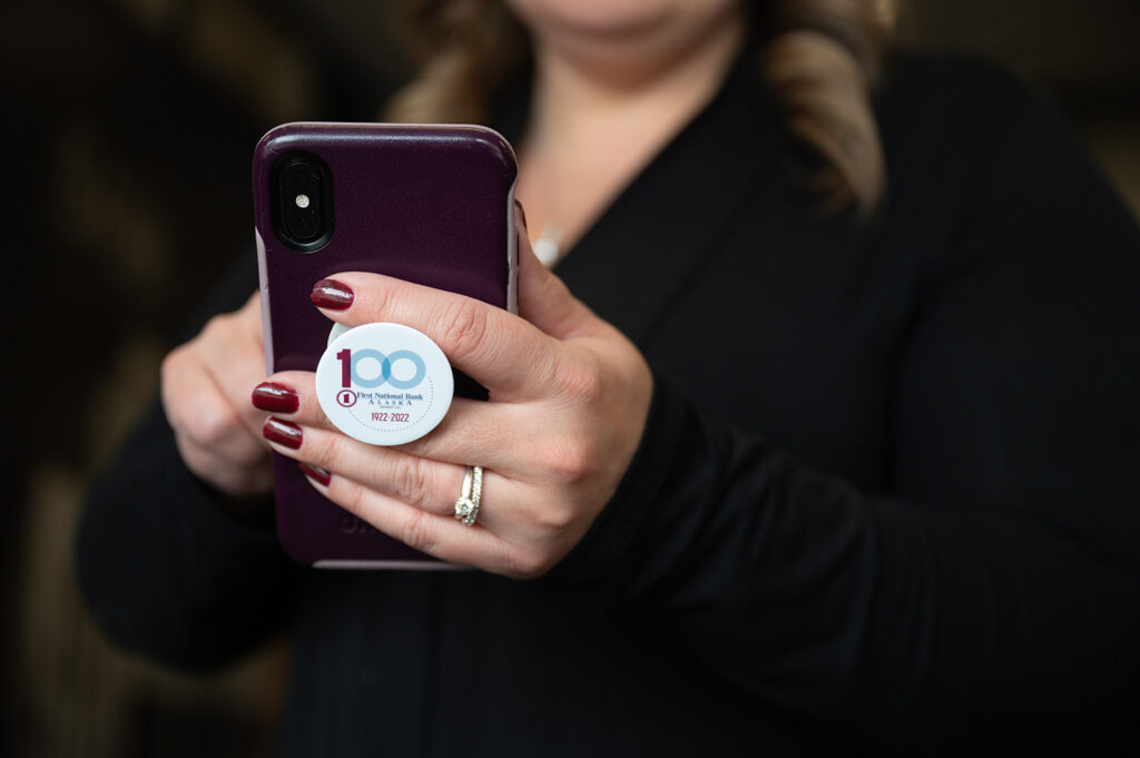 A woman stands with her smartphone in front of her, actively interacting with the device in her hands.