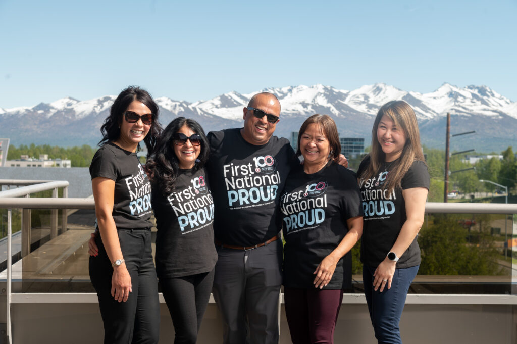 A group of four people stands together, each wearing a shirt that reads "First National Proud," symbolizing excellence and camaraderie.