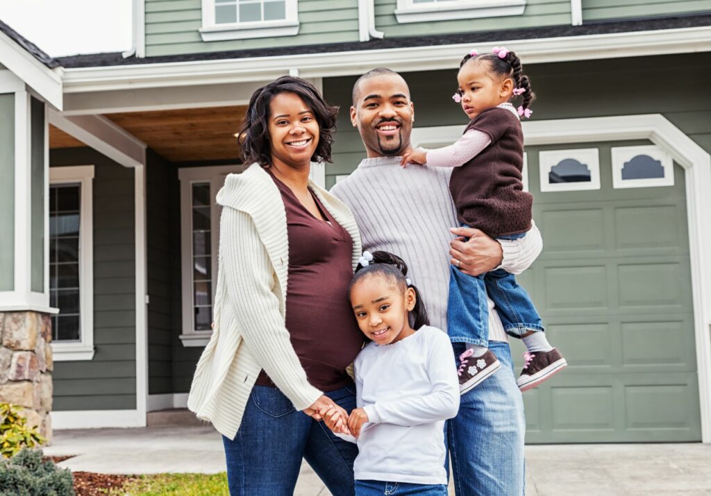 A happy family poses in front of their new house, showcasing their excitement and pride in their recent home purchase.