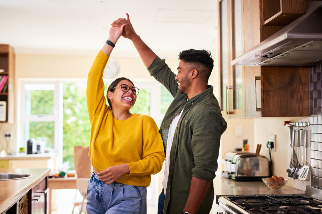 In a kitchen, a man and woman enthusiastically raise their hands, expressing joy and togetherness.