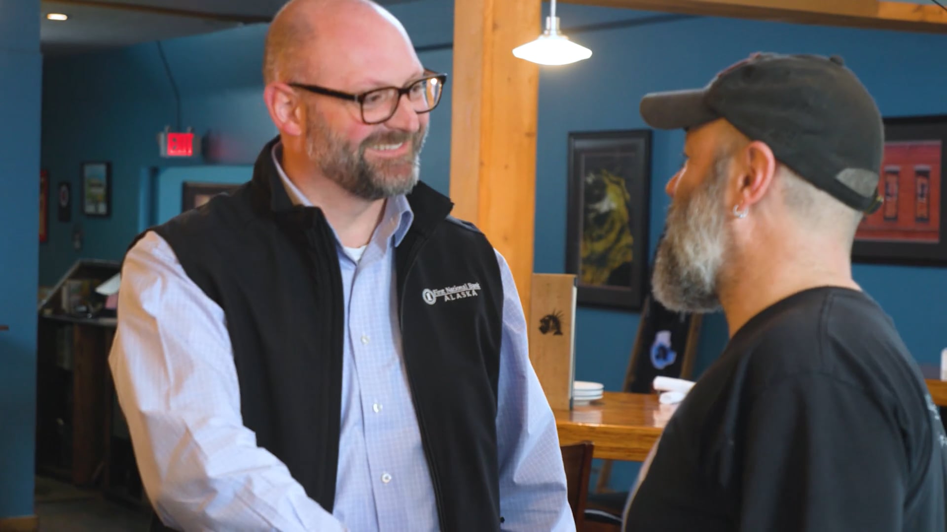 Two men engage in a handshake, one with a beard and glasses, representing a moment of collaboration or mutual respect.