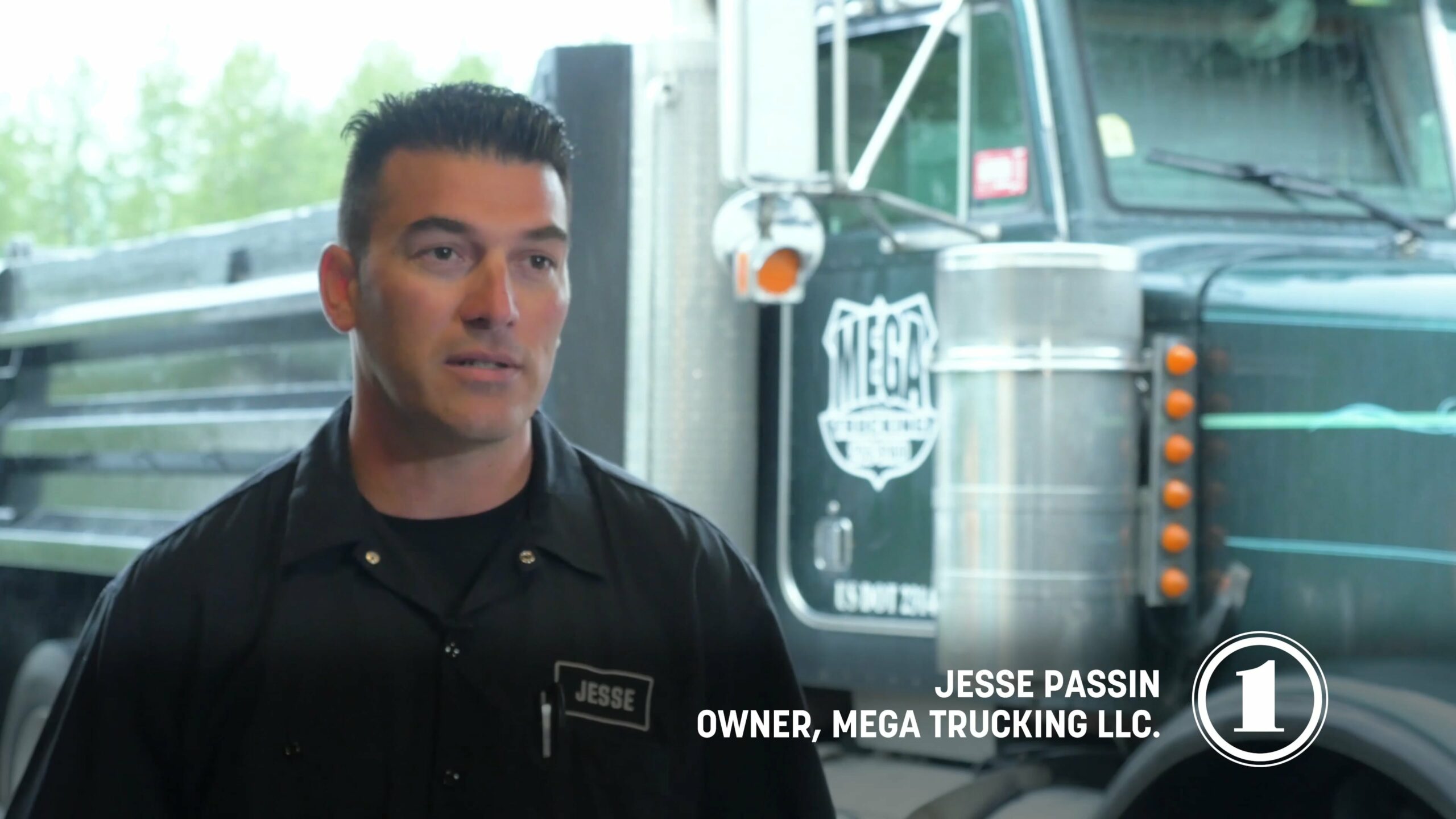 A man wearing a black shirt stands next to a truck, exuding a relaxed and approachable presence in a natural environment.