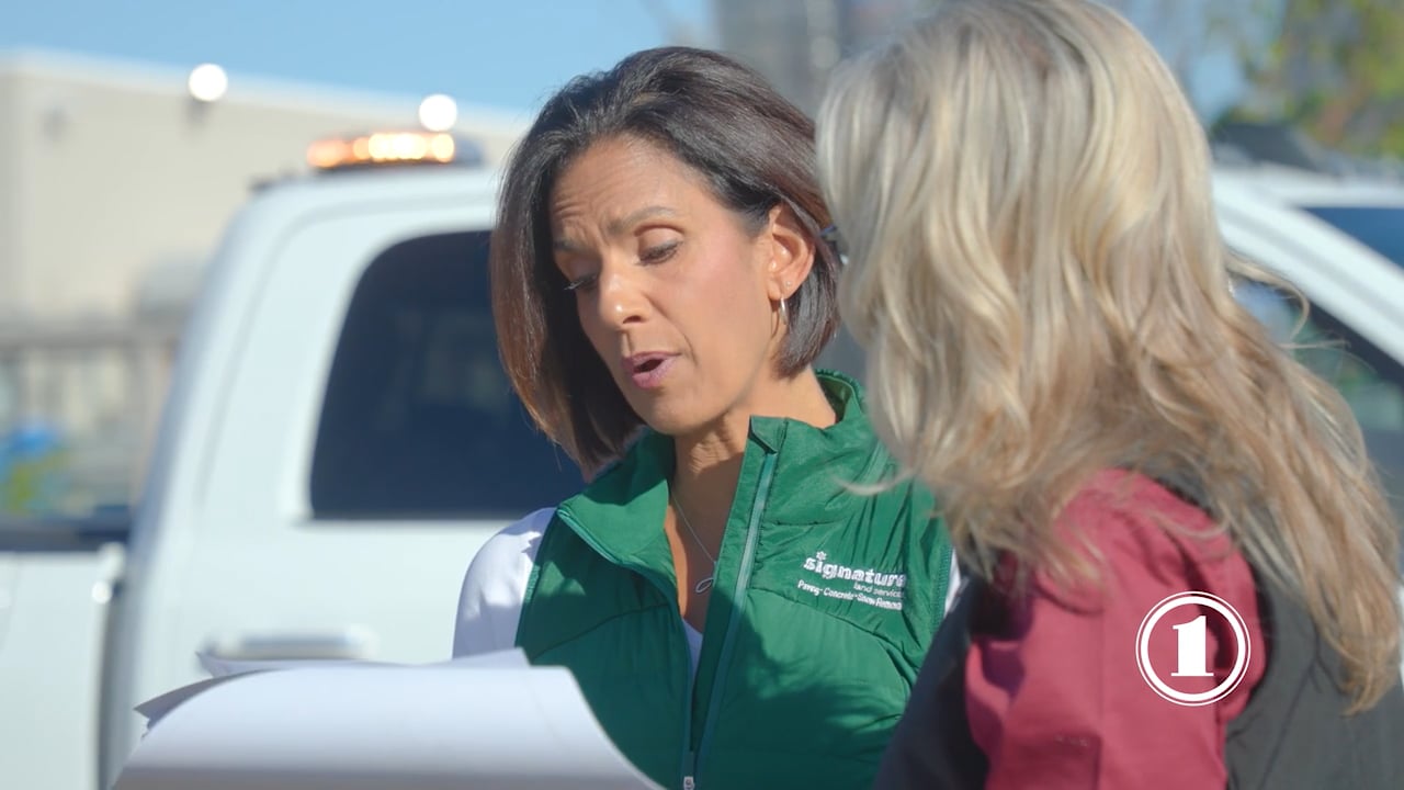 Two women in green vests engage in conversation with a truck driver beside his vehicle.