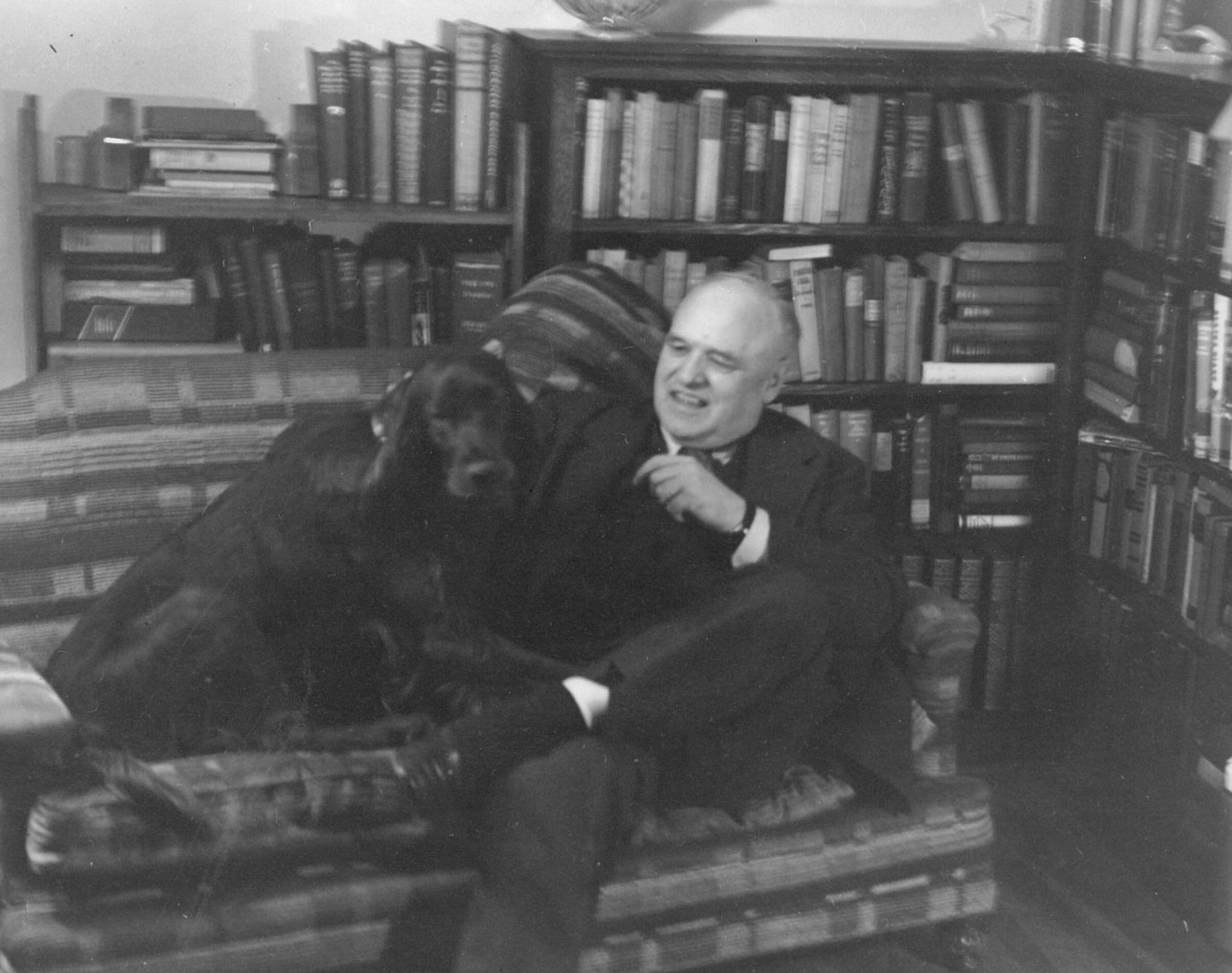 A photo of Warren Cuddy sitting next to a bookshelf.