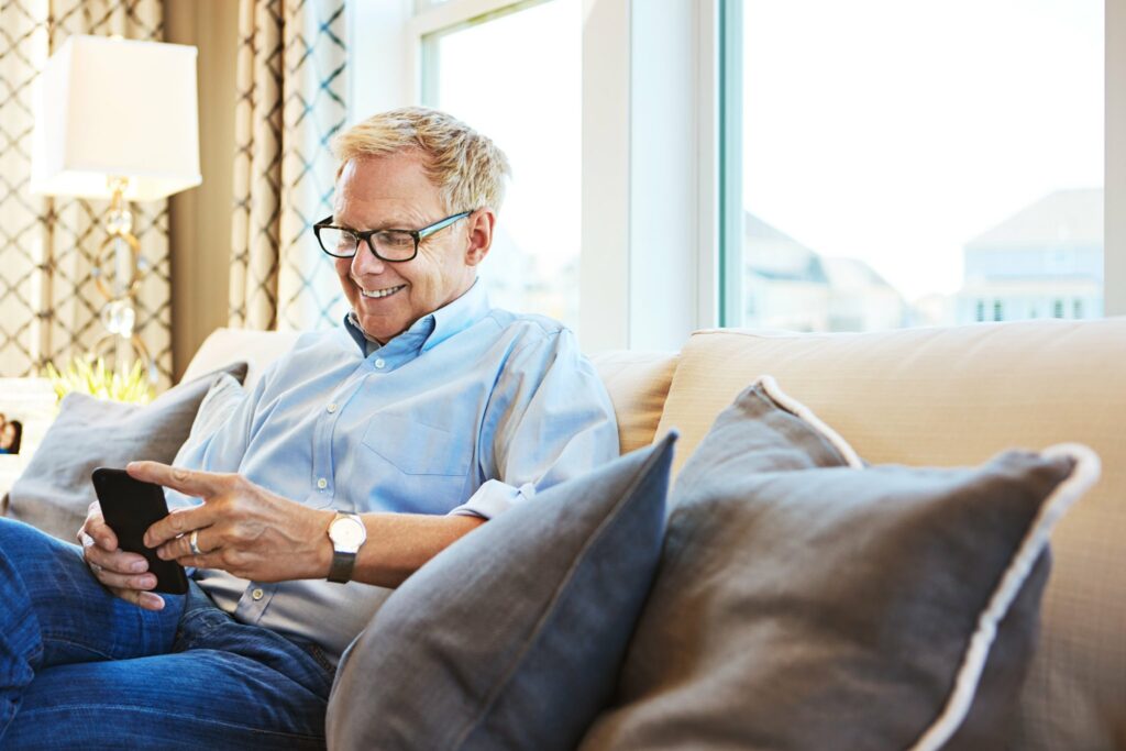 A man comfortably sitting on a couch, engaged with his smartphone