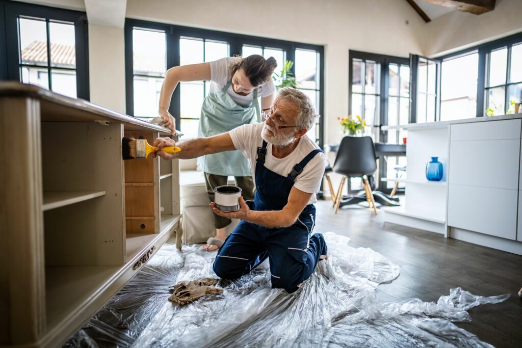 A man and woman collaborate on painting their kitchen as part of their home renovation project.