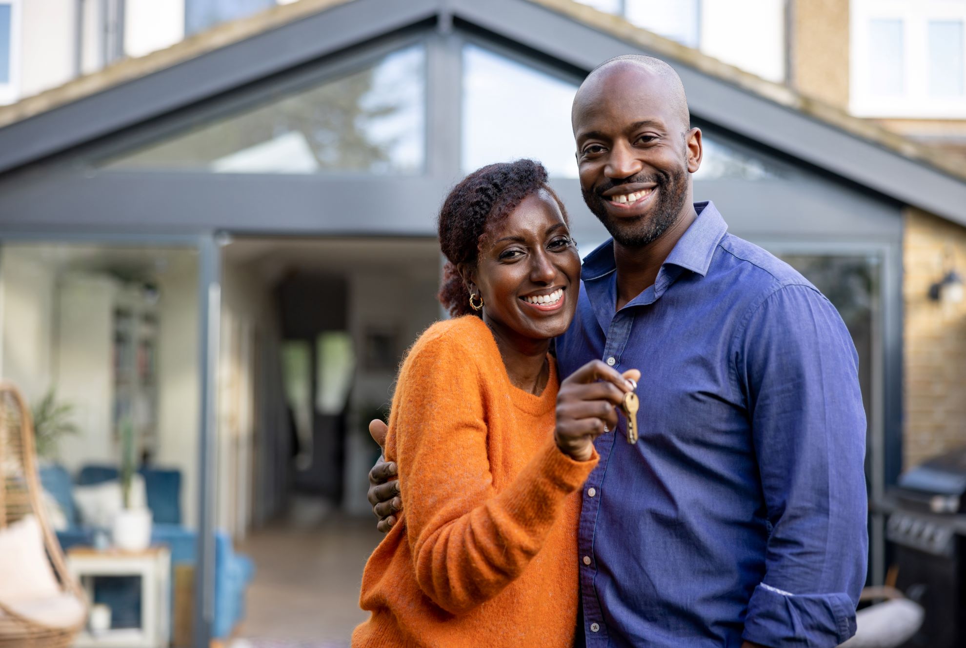 A couple smiles as they hold keys in front of their new home, celebrating the milestone of homeownership and their journey ahead.